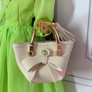May include: A white handbag with gold handles and a bow detail. The bag has a textured finish and a tassel.