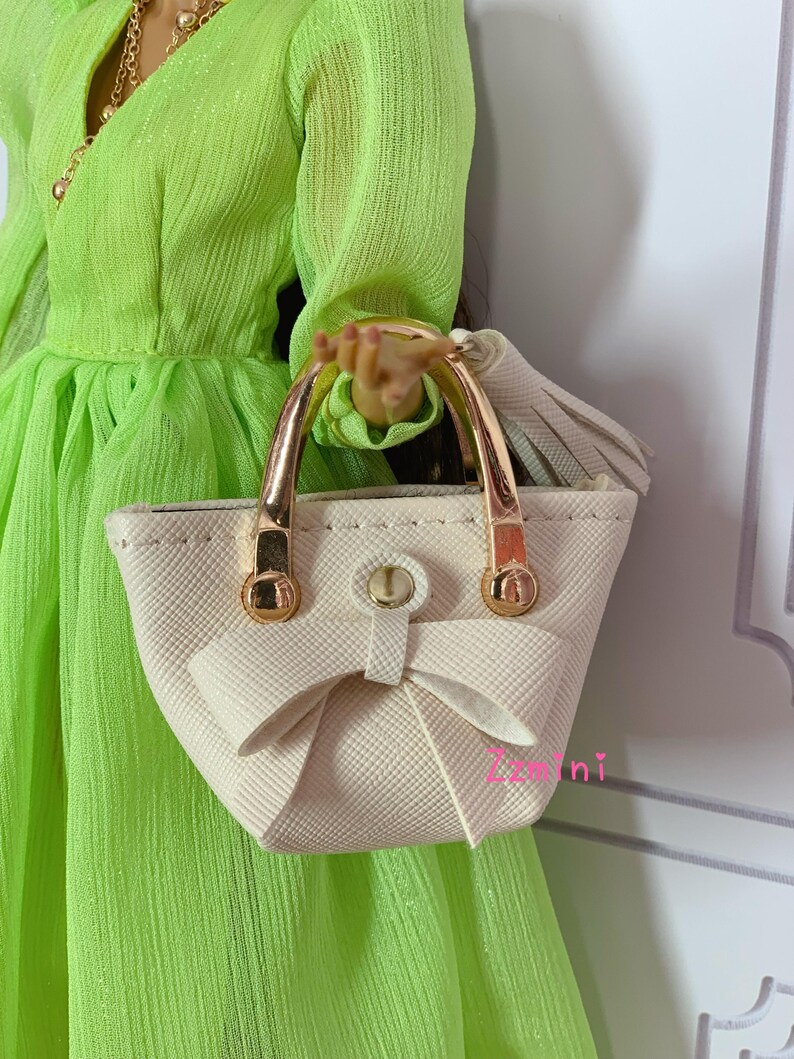 May include: A white handbag with gold handles and a bow detail. The bag has a textured finish and a tassel.