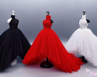 May include: Three miniature doll dresses in black, red, and white, each featuring a high-neck bodice with intricate detailing and a voluminous, layered tulle skirt with a high-low hemline. The dresses are displayed on individual stands.