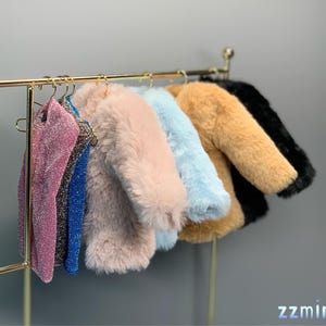 May include: A rack of clothing with six items hanging on hangers. The items include a pink, blue, and brown faux fur jacket, a light blue jacket, a black jacket, and two sparkly tops.