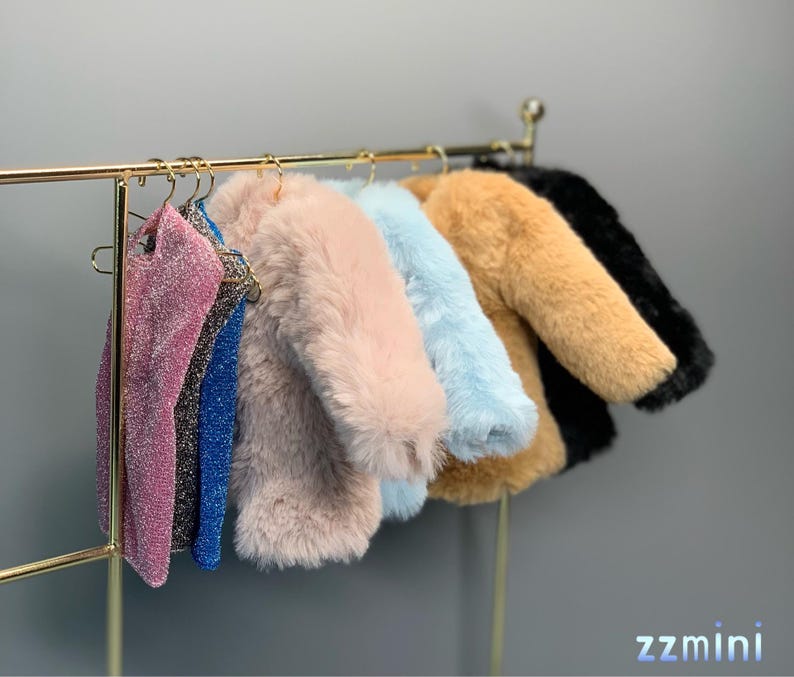 May include: A rack of clothing with six items hanging on hangers. The items include a pink, blue, and brown faux fur jacket, a light blue jacket, a black jacket, and two sparkly tops.