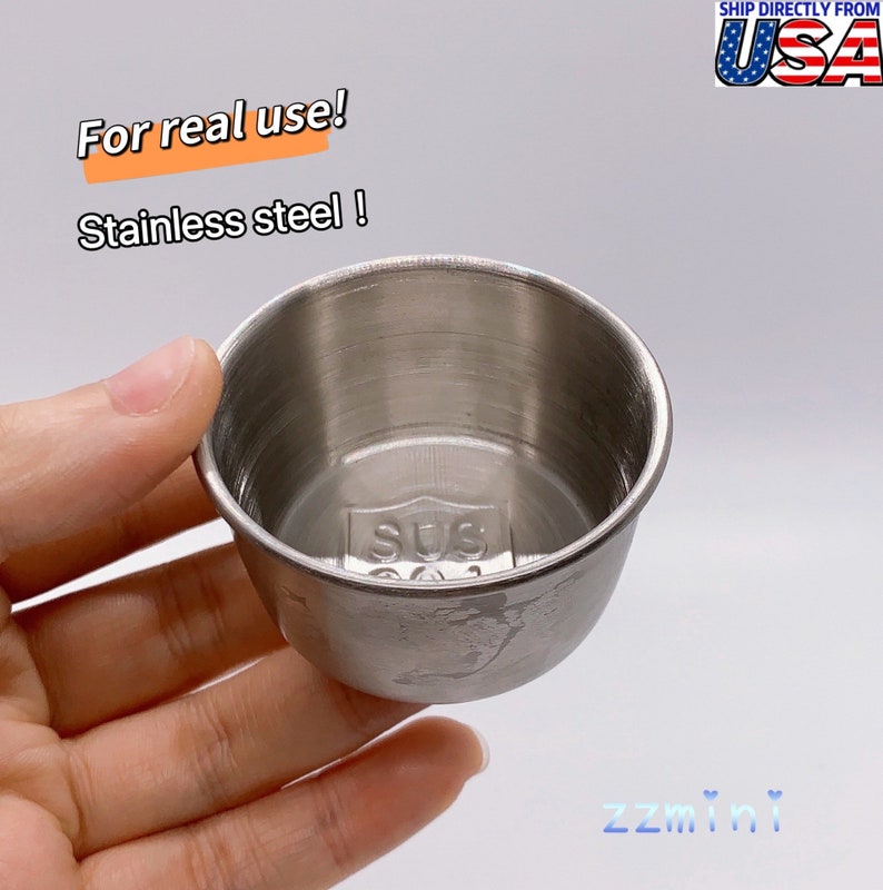 May include: A small, silver, stainless steel cup with a rounded bottom and a lip around the top. The cup has a small, embossed label on the bottom that says "SUS 304".