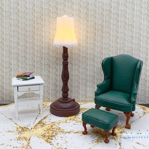 Pu&ograve; includere: Una lampada bianca in miniatura con un paralume color crema si trova su un tappeto bianco accanto a un tavolino bianco con un cassetto. Una poltrona verde con un poggiapiedi abbinato si trova sul tappeto.