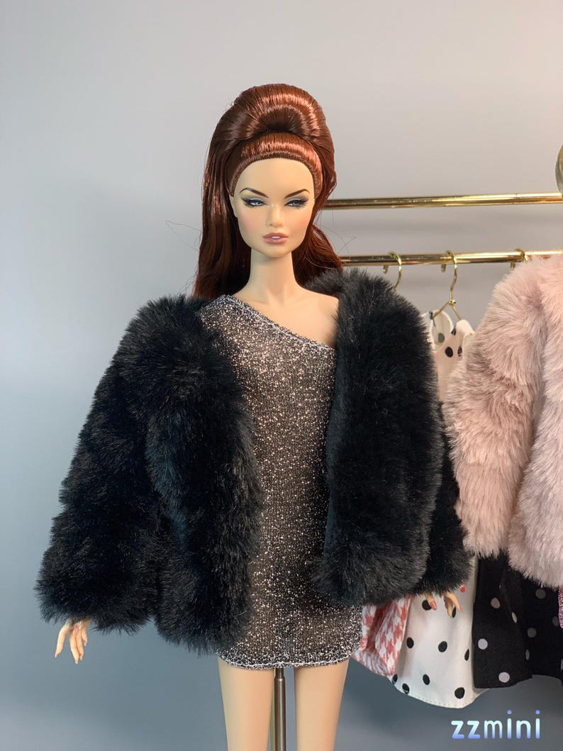 May include: A black faux fur jacket with a silver sparkly dress underneath. The doll is wearing a high bouffant hairstyle.