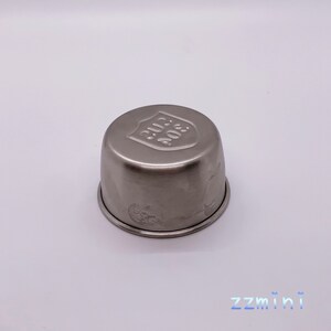 May include: A silver metal cup with a rounded top and a raised shield design on the top. The shield has the text "304 SUS" embossed on it.