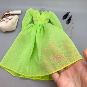 May include: A lime green chiffon dress with a V-neckline and long sleeves. The dress has a gathered skirt and a yellow trim. The dress is on a white surface.