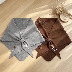 May include: Two triangular scarves, one in heather gray and one in dark brown, each featuring a small brown leather-like tag and white embroidered initials. The gray scarf displays the letters ERT, while the brown scarf displays the letters GLS.