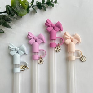 May include: Four clear drinking straws with colorful bow-shaped tops and gold charms with letters 'A', 'P', 'D', and 'C' attached.