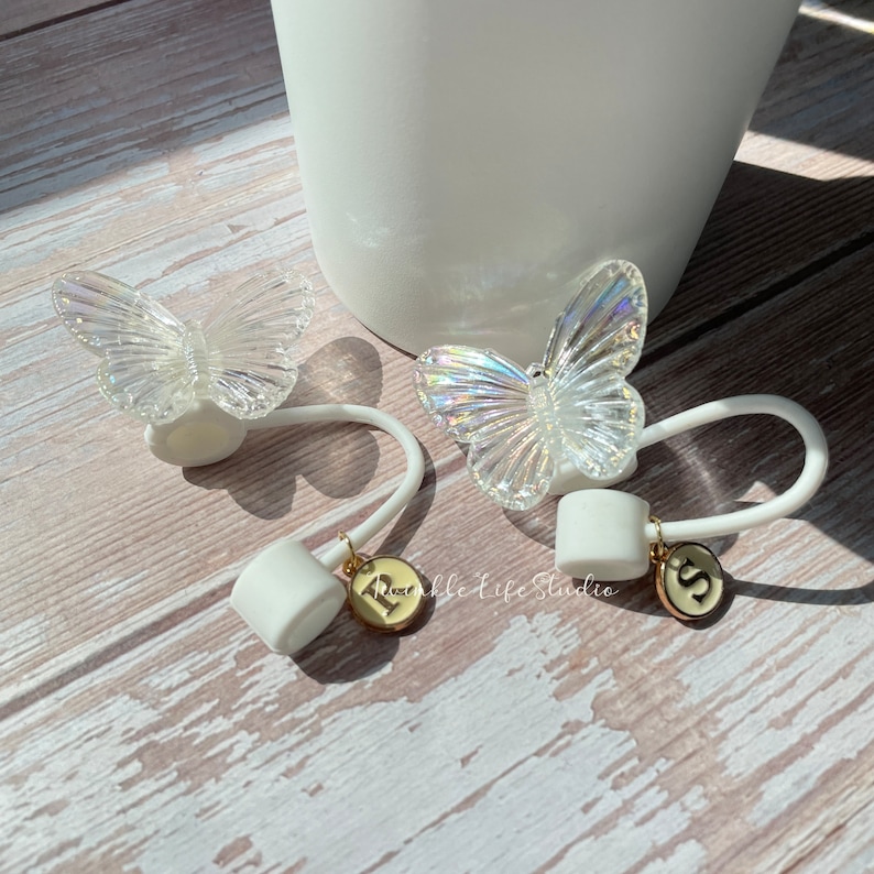 Puede incluir: Dos gomas para el pelo de silicona blanca con abalorios de mariposa iridiscente. Cada goma tiene un abalorio dorado con una letra, uno con una "R" y el otro con una "S".