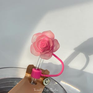 May include: A pink rose-shaped straw topper with a pink silicone straw holder and a gold charm with the letter "C" on it.
