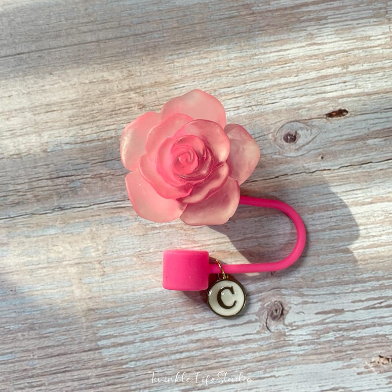 May include: A pink silicone rose-shaped bottle stopper with a pink silicone loop and a gold charm with the letter "C" on it.
