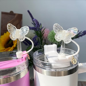 Puede incluir: Dos tazas de viaje de acero inoxidable con tapas transparentes y tapas de pajita de mariposa. Las tazas son de color rosa y blanco. Las tapas de pajita de mariposa son iridiscentes y tienen un encanto unido a la pajita.