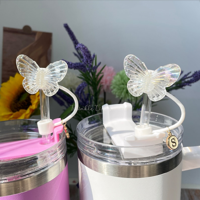 Puede incluir: Dos tazas de viaje de acero inoxidable con tapas transparentes y tapas de pajita de mariposa. Las tazas son de color rosa y blanco. Las tapas de pajita de mariposa son iridiscentes y tienen un encanto unido a la pajita.