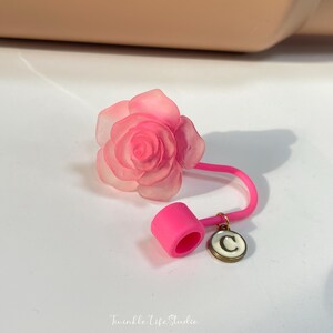 May include: A pink silicone rose-shaped bottle stopper with a pink silicone ring and a gold charm with the letter "C" in white.
