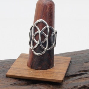 Könnte beinhalten: Ein silberner Ring mit geometrischem Design. Der Ring befindet sich auf einem hölzernen Ringständer.