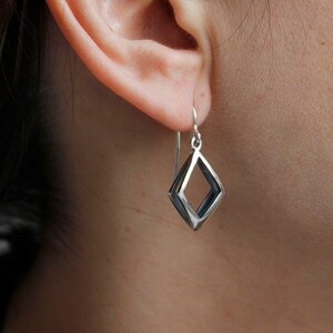 May include: Silver earrings with a geometric diamond shape design. The earrings are made of a single piece of metal that is bent to create the shape.