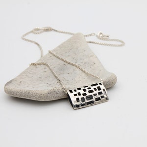 May include: A silver necklace with a geometric pendant. The pendant is a rectangular shape with a cut-out design. The necklace is on a white background.