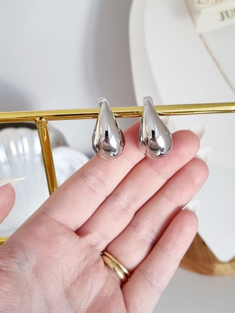 K&ouml;nnte beinhalten: Ein Paar silberne Ohrringe in Tropfenform. Die Ohrringe sind glatt und gl&auml;nzend.