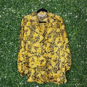 May include: A black and gold long-sleeved button-up shirt with a paisley pattern.