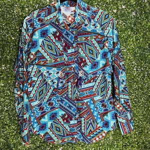 May include: A long-sleeved shirt with a striking geometric design in blue, red, and green. The shirt has a traditional collar and button fastening. The material appears soft and drapes well.