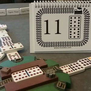 May include: A white domino set with a train track design on the game board. The dominoes are arranged in a line, with the number 11 on the game board. The game board is made of wood and has a green base.