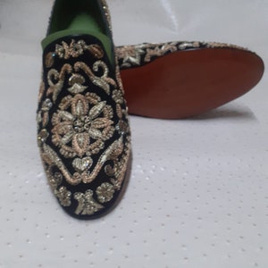 Puede incluir: Un par de mocasines de terciopelo negro con bordados dorados y plateados. Los mocasines tienen una punta puntiaguda y un dise&ntilde;o de deslizamiento.