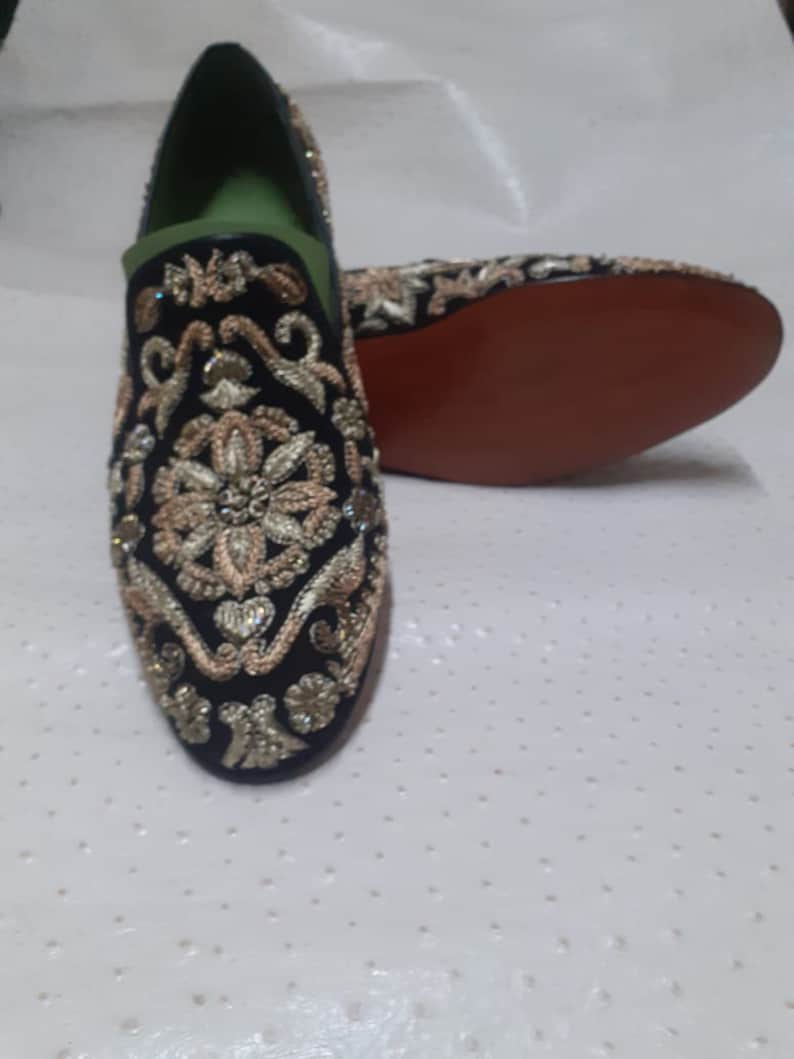Puede incluir: Un par de mocasines de terciopelo negro con bordados dorados y plateados. Los mocasines tienen una punta puntiaguda y un dise&ntilde;o de deslizamiento.