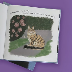 May include: An open book illustration featuring a tabby cat with a flowing mane, sitting on a gray surface. The cat is brown and tan with black stripes. Text above reads, "OR THIS PRETTY KITTY. LOOK AT HER BEAUTIFUL FLOWING MANE."