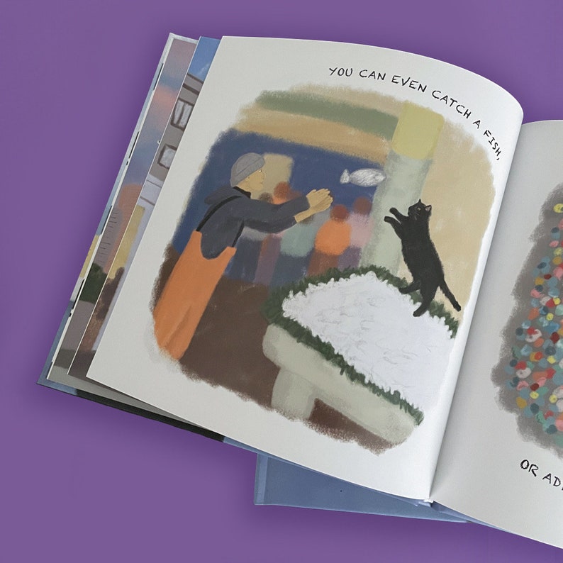 May include: An open children's book with colorful illustrations. One page shows a person in orange overalls and a black jacket reaching for a fish, with a black cat jumping nearby. The text reads, "YOU CAN EVEN CATCH A FISH,"