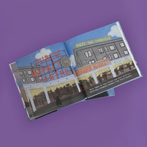May include: An open book with illustrations of Seattle's Pike Place Market. The left page features the words "Public Market Center" in red lettering. The right page shows a building with the words "Meet the Producer" and "Farmers Market". A black cat is in the foreground.
