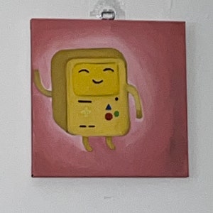 Puede incluir: Una pintura de un personaje de dibujos animados amarillo con una cara feliz y un mando de juego. El personaje está sobre un fondo rosa.