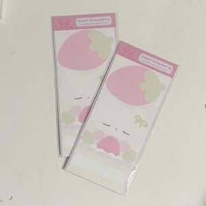 以下が含まれることがあります： ピンクのイチゴのデザインと「sweet strawberry」の文字が入った長方形のステッカーシートが2枚。ステッカーには、ピンクのイチゴ、緑の葉、リボンが付いた、かわいい漫画のキャラクターデザインが施されています。「chez loopy」のブランド名も表示されています。