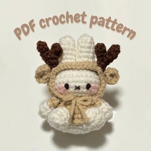 May include: A crocheted amigurumi reindeer bunny wearing a brown hooded sweater with antlers. The bunny has a white body and brown eyes. The text "PDF crochet pattern" is written above the bunny.