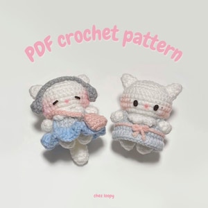 May include: Two crocheted cat plushies wearing blue and pink outfits. The plushies have white fur, pink cheeks, and black eyes. The text "PDF crochet pattern" is written in pink letters at the top of the image.