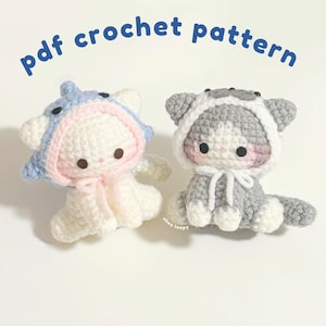 May include: Two small crocheted cat figures with hoods, one white with a blue hood and one gray with a white hood, featuring dark eyes and pink cheeks. The text 'pdf crochet pattern' is arched above, and 'chez loopy' is printed near the base.