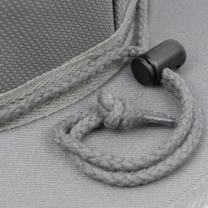 May include: A grey hat featuring a woven fabric texture and a matching grey drawstring cord. The cord is secured with a black plastic toggle fastener and is tied into a small knot, resting against the brim of the hat for adjustable fit.