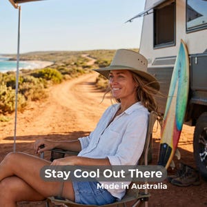 May include: A woman wearing a khaki-colored hat and white shirt sits in a folding chair outdoors. The text "Stay Cool Out There" and "Made in Australia" are visible. A surfboard leans against a camper.