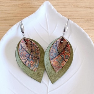 Puede incluir: Un par de pendientes de cuero verde con un diseño estampado de colores. Los pendientes tienen forma de hoja y tienen ganchos plateados.