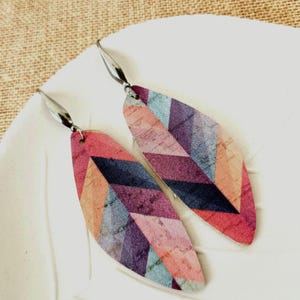 May include: A pair of long, teardrop-shaped earrings with a geometric pattern in shades of pink, purple, blue, and orange. The earrings have silver hooks.