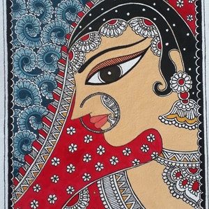 May include: An Indian-style painting featuring a woman's profile. The artwork showcases a red veil adorned with white floral patterns, a large nose ring, and elaborate jewelry. The background has blue floral patterns. The painting is signed "Anuja's Paintings".