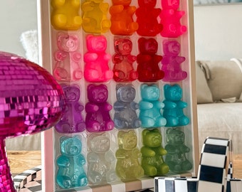 May include: A framed wall art piece featuring a grid of colorful gummy bear sculptures. The bears are arranged in a rainbow pattern, with each row featuring a different color.