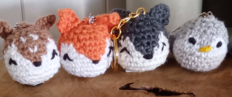 May include: Five crocheted animal keychains. The keychains are a deer, fox, wolf, penguin, and a bird. The keychains are all white with different colored accents. The keychains are all about 3 inches tall.