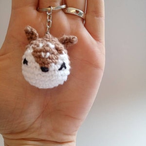 May include: A crocheted brown and white deer keychain with black eyes and a silver key ring.