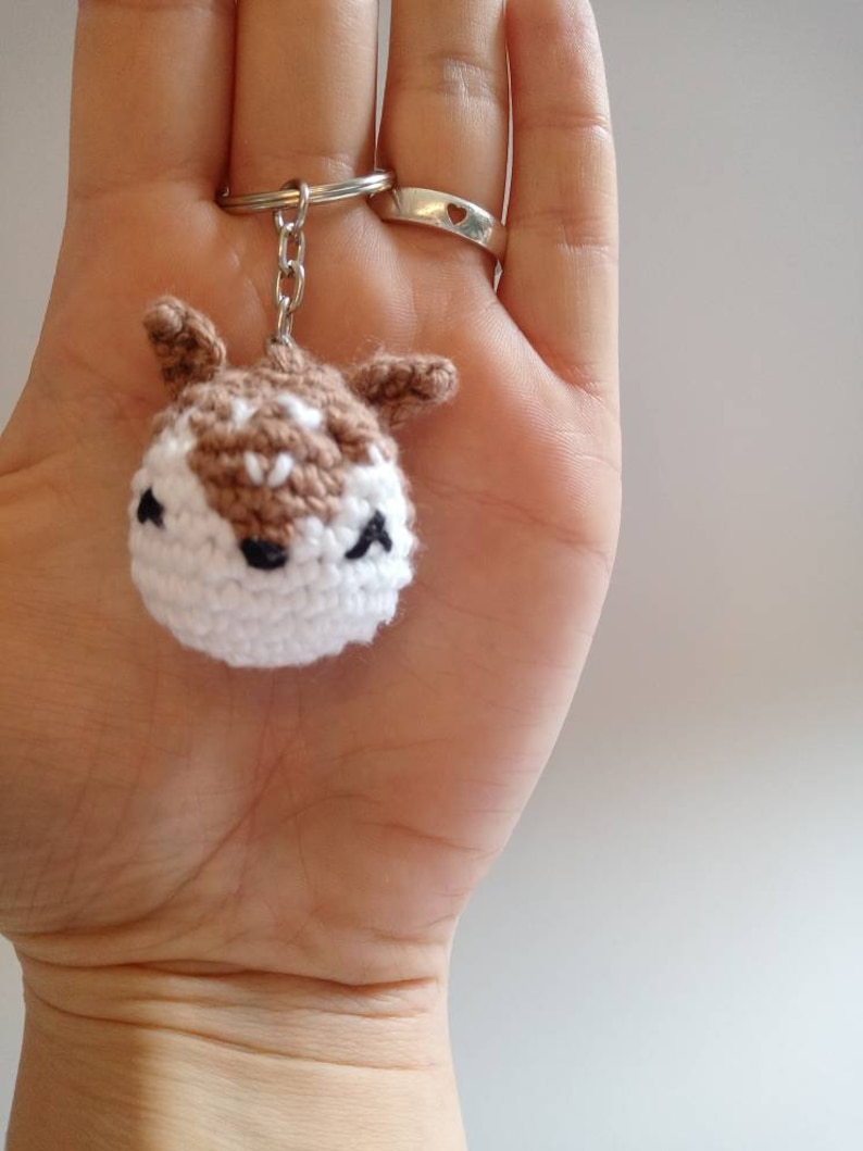 May include: A crocheted brown and white deer keychain with black eyes and a silver key ring.