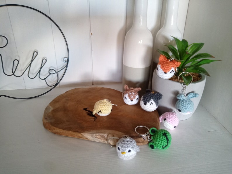May include: A collection of seven crocheted animal keychains. The keychains are in various colors, including yellow, orange, brown, gray, blue, pink, and green. The keychains are displayed on a wooden surface.