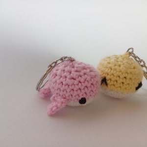 May include: Two crocheted keychains, one pink and one yellow, with black eyes. The keychains are shaped like small animals.