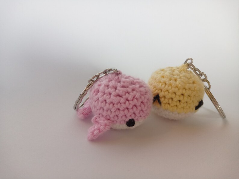 May include: Two crocheted keychains, one pink and one yellow, with black eyes. The keychains are shaped like small animals.