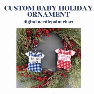 Puede incluir: Adornos navideños personalizados para bebés con forma de camisetas de bebé, uno a cuadros azules y otro a cuadros rojos, cada uno con un nombre y un año. Cuelgan de una corona de vegetación y bayas rojas. El texto en la parte superior dice "CUSTOM BABY HOLIDAY ORNAMENT".