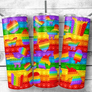 May include: Three cylindrical tumblers with lids and metal straws, featuring a vibrant rainbow-colored pop-it bubble pattern. The design includes various shapes like dinosaurs, hearts, unicorns, apples, cupcakes, and fries in bright colors.