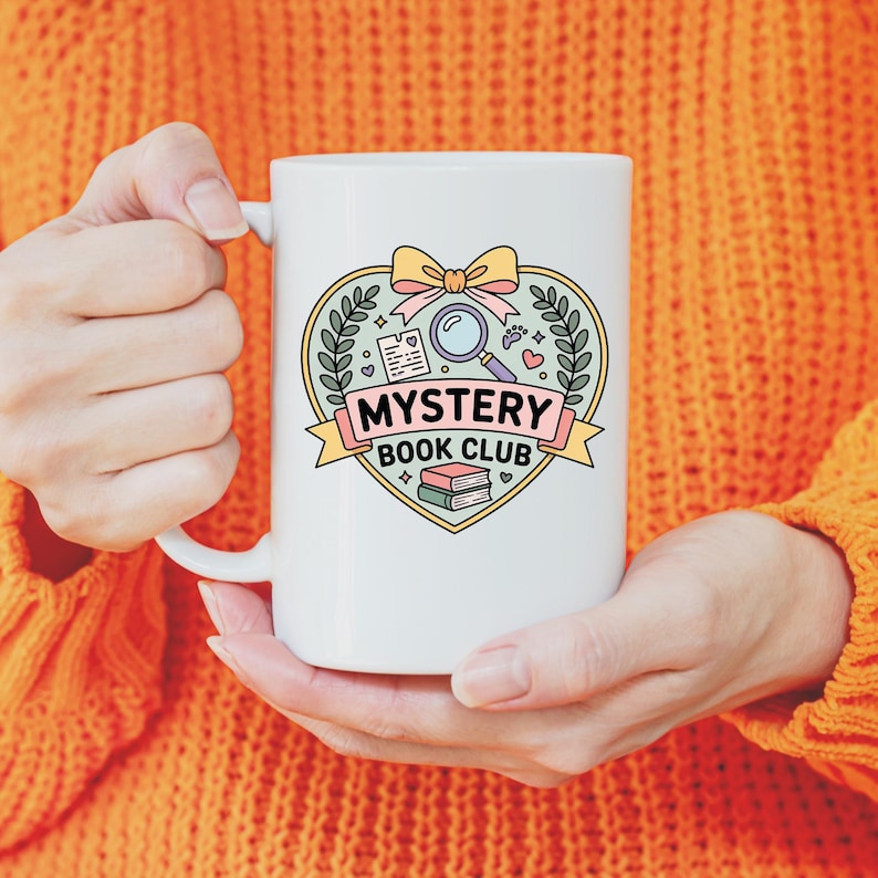 May include: White ceramic mug featuring a heart-shaped design with a magnifying glass, books, and the text "MYSTERY BOOK CLUB." The design includes a bow and laurel leaves. The mug is held by a person wearing an orange sweater.